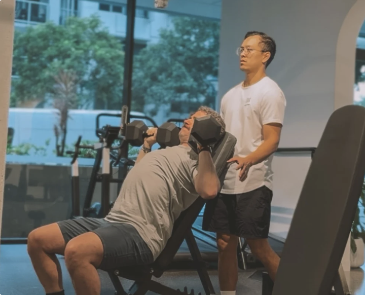 Dave on the bench pressing dumbbells, with his Club Crux coach standing behind him.