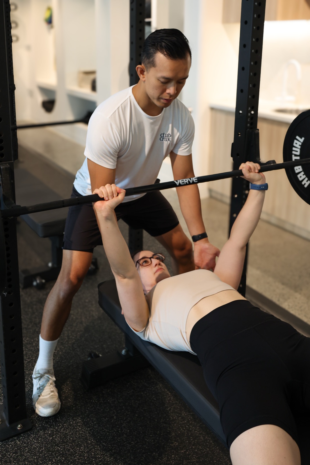 A Club Crux coach spotting a member through her bench press